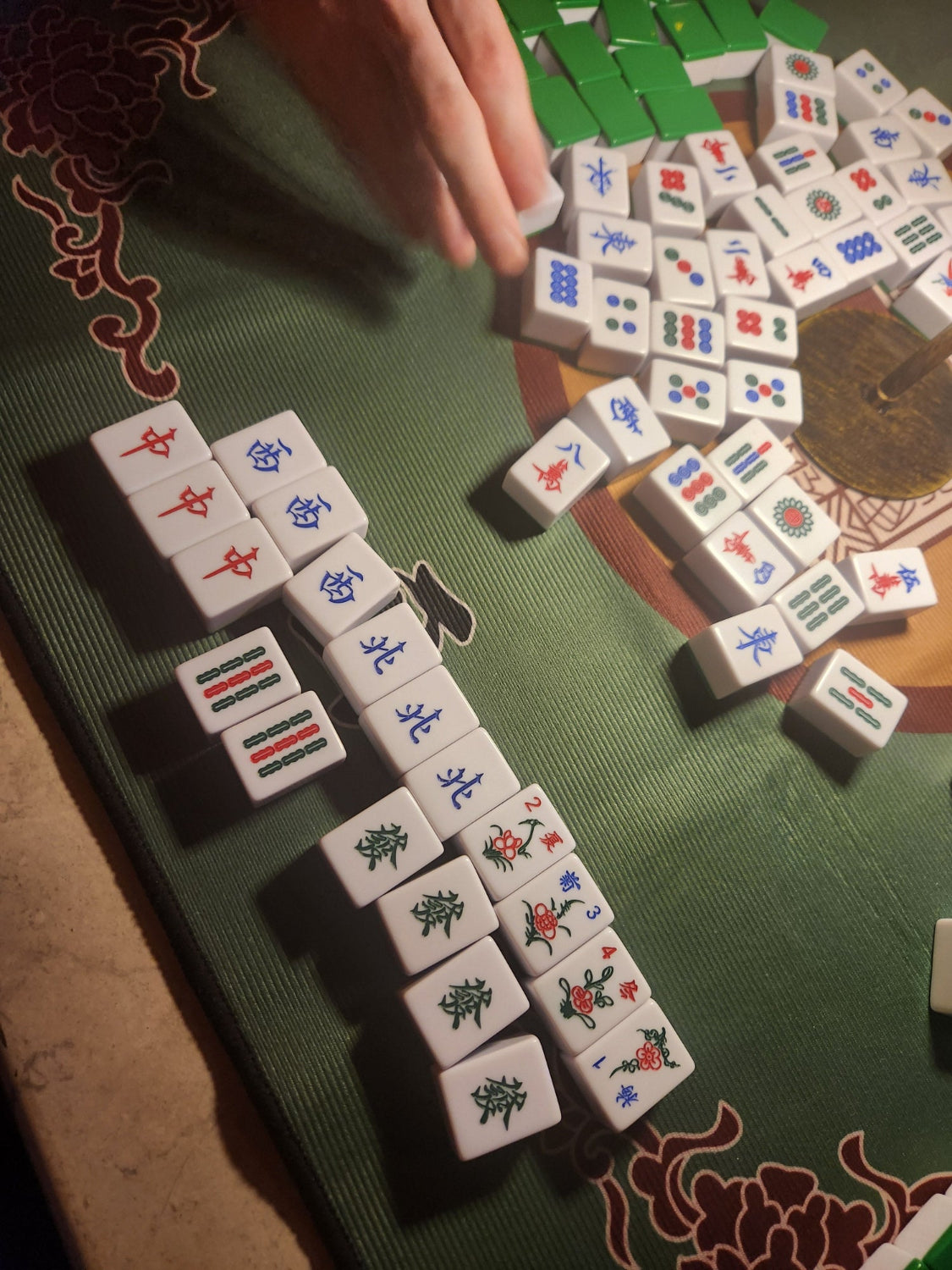 Mahjong game in progress on a green table with tiles and hand visible